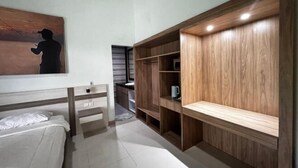 A bedroom with a bed, a wooden wardrobe, a painting, and a desk with a chair.