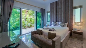 Un dormitorio con una cama grande, un sofá, una mesita de noche y vistas al exterior con vegetación.