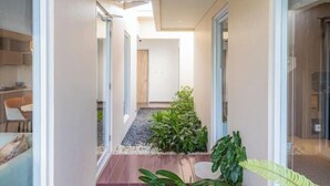 Ein moderner Flur mit Glastür zu einem Zimmer, ein kleiner Gartenbereich mit Pflanzen und ein Holzboden.