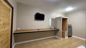 A room with a wooden floor, a built-in bench, a flat-screen TV mounted on the wall, and a small refrigerator. - IUnn Resort (Rayong)