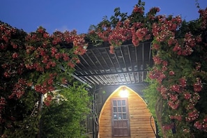 A wooden cabin with a covered entrance, surrounded by flowering vines.