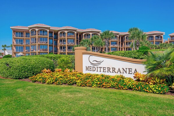 Un letrero de hotel con la palabra 'Mediterranea', rodeado de jardines florales y follaje cuidado.