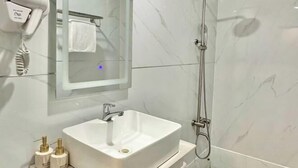 Ein Badezimmer mit einem weißen Waschbecken, einer Handbrause und einem an der Wand befestigten Föhn.