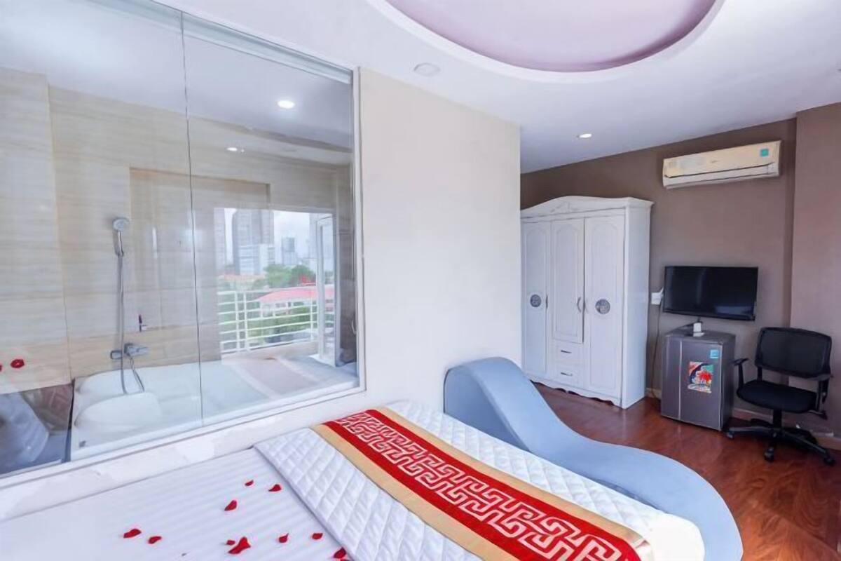 A hotel room with a glass shower, a bed with rose petals, a TV, and a wardrobe.
