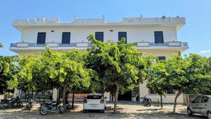 A hotel with a flat facade, multiple windows, and a parking area with motorcycles and cars. - Hare Krishna Hotel & Restaurant (Phulera)