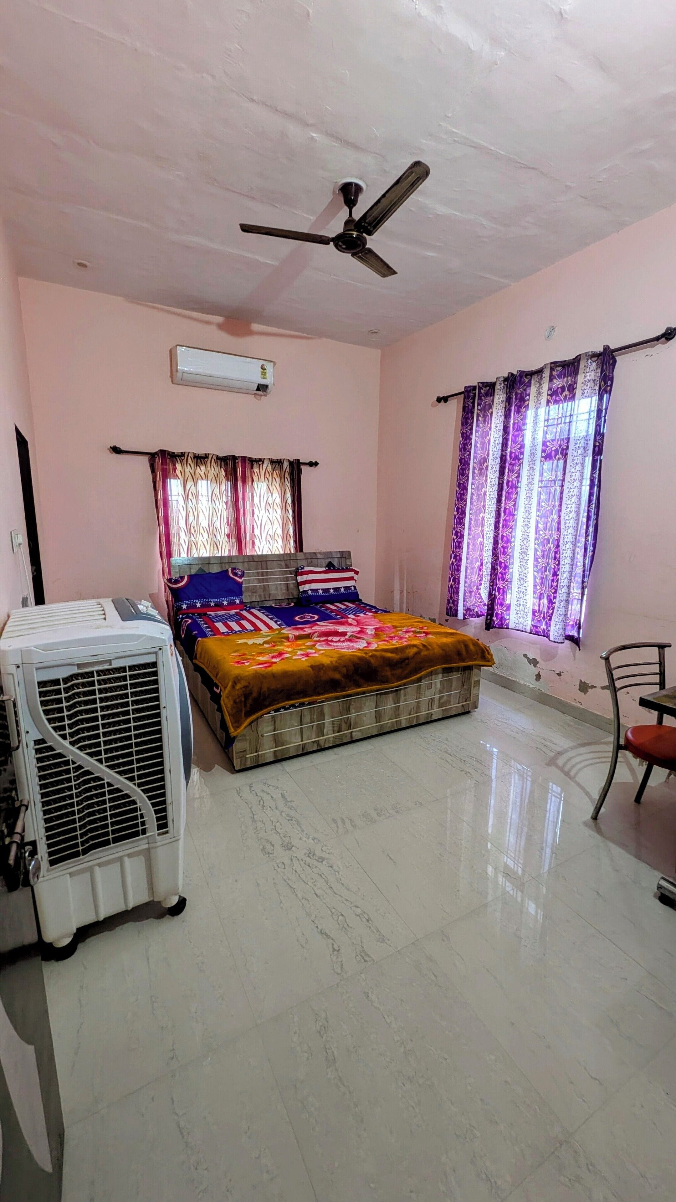 Un dormitorio con cama, ventilador de techo, aire acondicionado y ventana con cortinas.