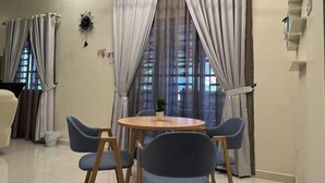 A dining area with a round wooden table and four chairs, large windows with curtains, and a wall-mounted clock. - Entire Vacation House In Sitiawan (Sitiawan)