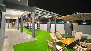 A modern outdoor seating area with a green artificial turf, wooden tables, and chairs. - Entire Vacation House In Sitiawan (Sitiawan)