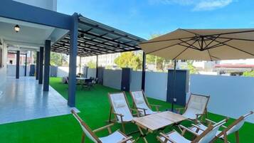 An outdoor patio with a covered seating area, artificial turf, and a clear sky.