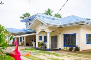 A two-story house with a blue roof and white walls, featuring a covered porch and a small garden area. - Sunrise Guesthouse & Inn, Panglao (Panglao)