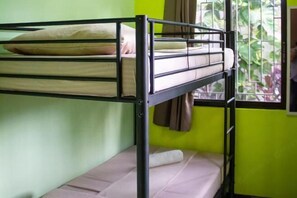 Una cama litera con colchón y almohadas, una ventana con cortinas y una pared verde.