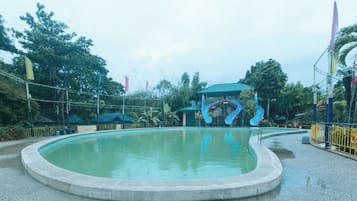 A circular pool with a water slide, surrounded by a fence and trees.