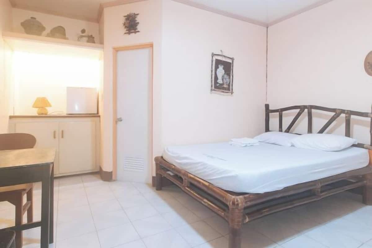 A bedroom with a wooden bed, a desk with a chair, a wardrobe, and a small wall-mounted shelf.