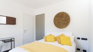 A bedroom with a bed, a bedside table, a mirror, and a wall-mounted circular artwork. - Lovely Apartment Overlooking the Lake (Carate Urio)