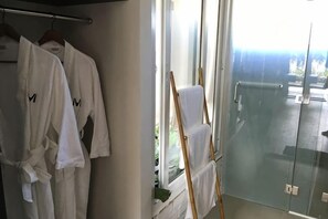 A hotel room with a glass shower door, a wooden chair, and white bathrobes hanging on a rack. - M Villa Nha Trang (Nha Trang)