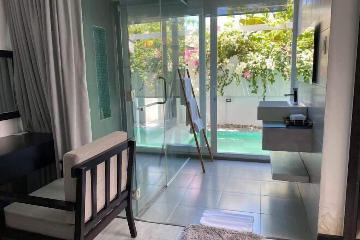 Un baño moderno con puerta de cristal, un lavamanos pequeño y una silla.