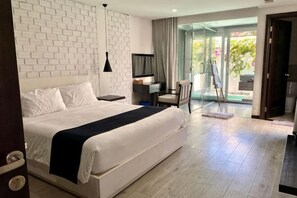 Una habitación de hotel moderna con una cama grande, un escritorio, una silla, un televisor y un ventanal de vidrio que da a un balcón.