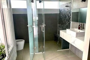 Un baño moderno con cabina de ducha de vidrio, un lavabo blanco y zona de ducha con azulejos.