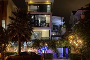 Un moderno edificio de dos pisos con balcones, un coche estacionado adelante y luces decorativas.