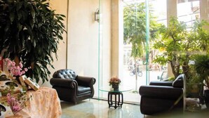 A lobby with a glass partition, a leather sofa, a small round table with a vase, and large potted plants. - NEW CENTURY HOTEL LANG SON (Lang Son)