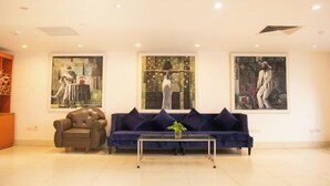 A modern living room with a dark blue sofa, a leather armchair, and a coffee table. There are three large abstract paintings on the wall. - NEW CENTURY HOTEL LANG SON (Lang Son)