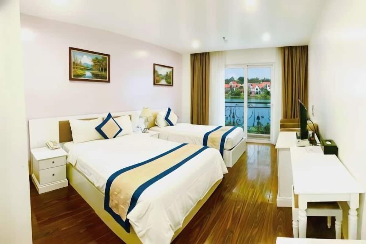 Quarto de hotel com duas camas, uma escrivaninha e varanda com vista.