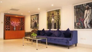 A modern living room with a blue sofa, a glass coffee table, and a wooden cabinet with wine bottles. - NEW CENTURY HOTEL LANG SON (Lang Son)