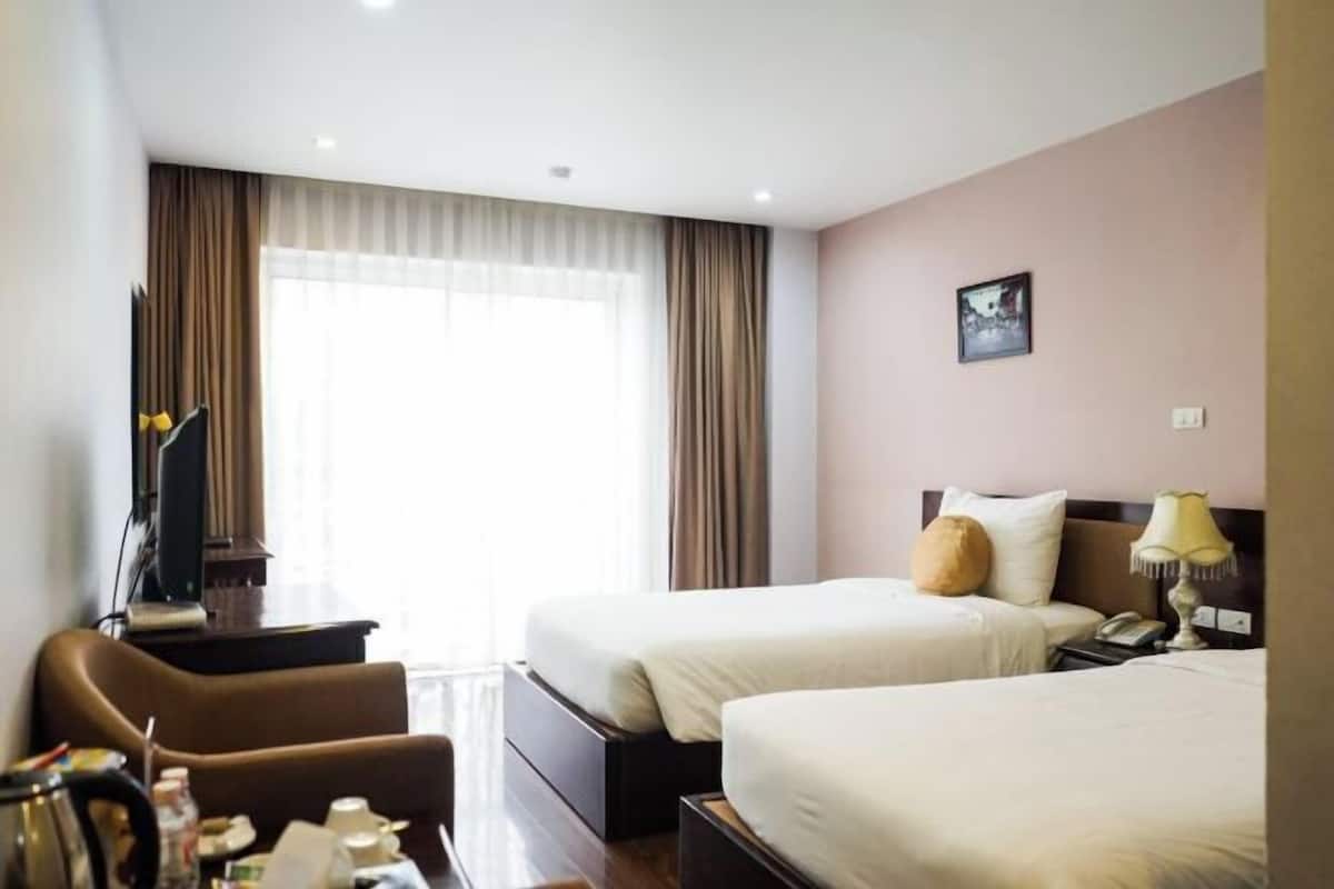 Quarto de hotel com duas camas, uma escrivaninha, uma cadeira, televisão e janela com cortinas.