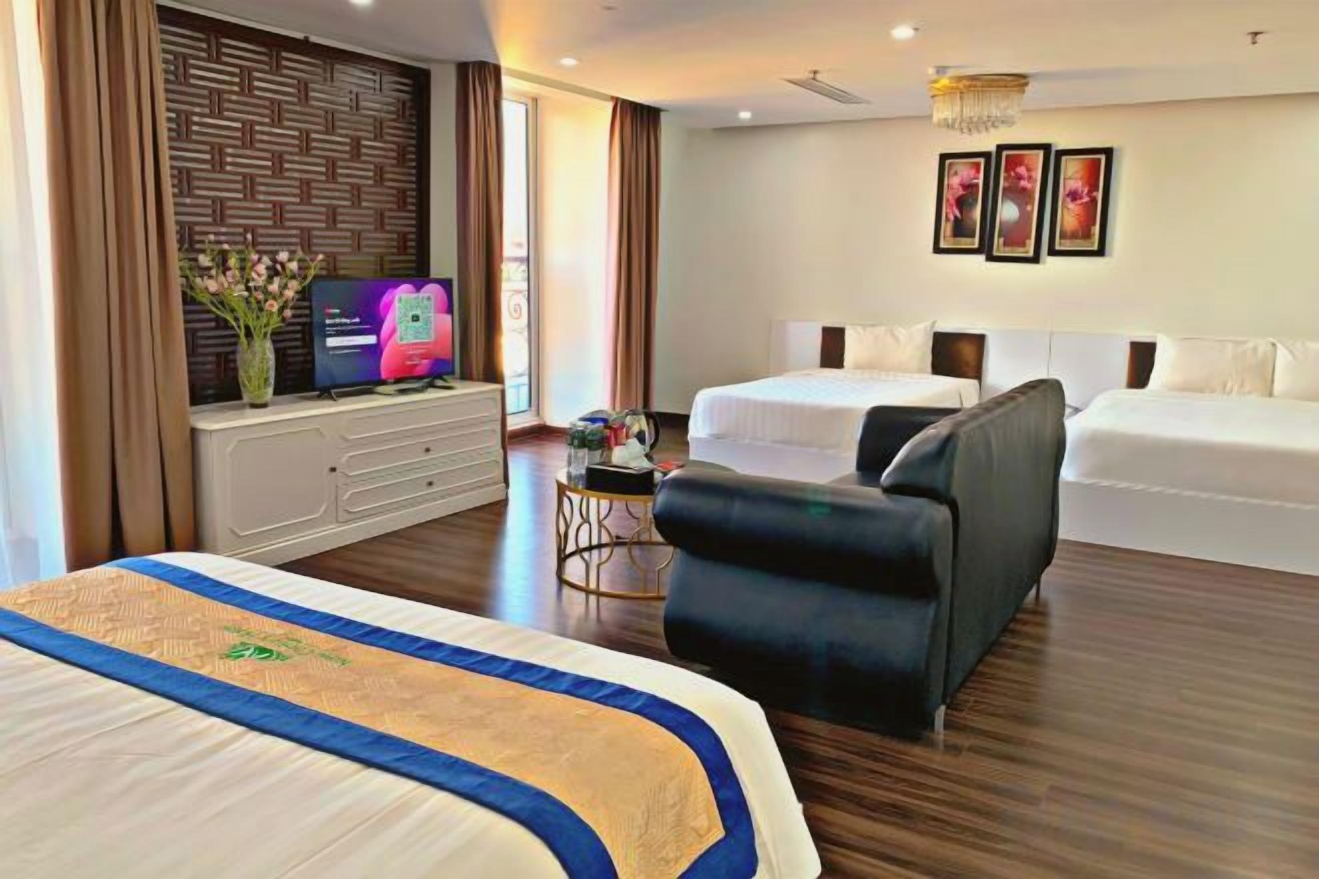 Habitación de hotel con cama, sofá, televisión y escritorio con un jarrón de flores.