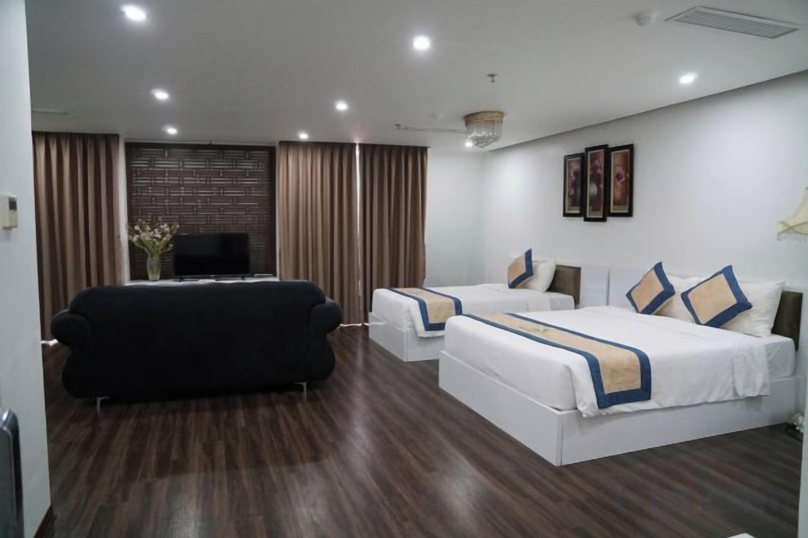 A hotel room with a sofa, two beds, a TV, and a wall-mounted TV.