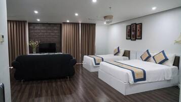 A hotel room with a sofa, two beds, a TV, and a wall-mounted TV.