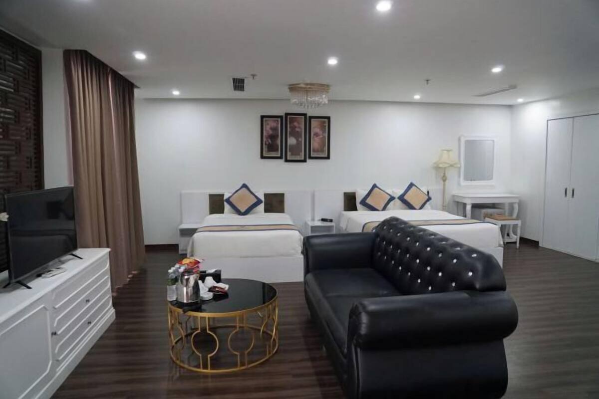 Quarto de hotel com uma cama grande, um sofá, uma TV e uma pequena mesa.