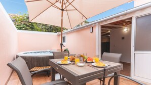 Une terrasse avec une table mise pour le petit-déjeuner, comprenant des assiettes de nourriture, des verres de jus d’orange et un jacuzzi en arrière-plan.