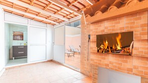 Une vaste terrasse dotée d’une cheminée en briques, d’une porte-fenêtre coulissante donnant sur un balcon et d’un sol carrelé.
