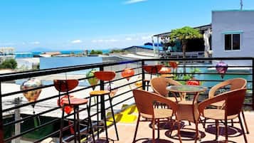 Una terraza con sillas de mimbre y una mesa, con vistas a un cuerpo de agua y edificios.