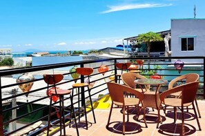 A terrace with wicker chairs and a table, overlooking a body of water and buildings.