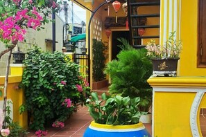 A courtyard with potted plants, a yellow wall, and a tiled floor. - Phở Homestay (Phan Thiet)