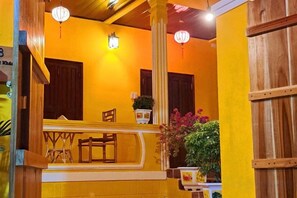A yellow-walled room with a wooden bench, a table, and a potted plant. - Phở Homestay (Phan Thiet)