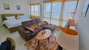 Ein Hotelzimmer mit Bett, Sofa, Couchtisch und einem großen Fenster mit Vorhängen.