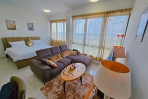 Hotellihuone, jossa on sänky, sohva, sohvapöytä ja suuri ikkuna, jossa on verhot.