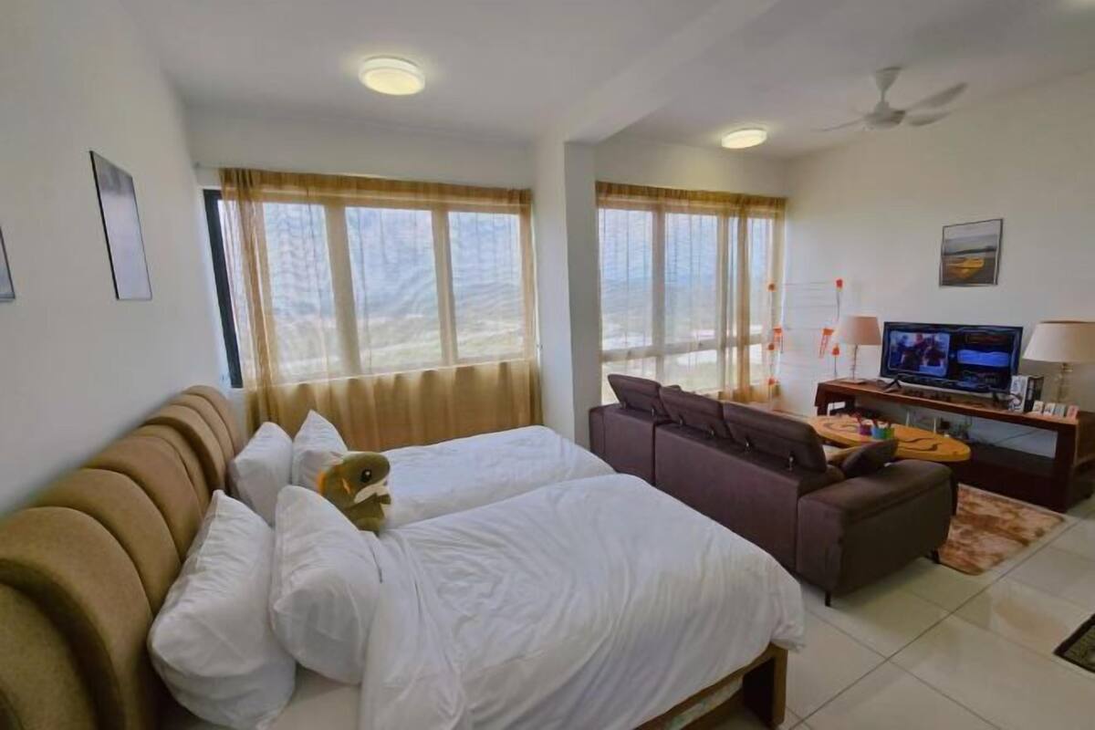 A hotel room with a bed, a sofa, a TV, and a window with curtains.