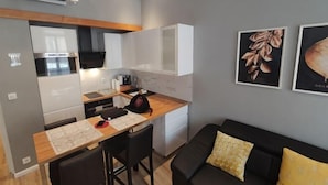 A compact kitchen with a dining area, a black couch with yellow pillows, and two framed pictures on the wall. - Apartment Centre Carmes (Toulouse)