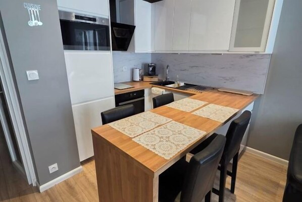 A compact kitchen with a wooden table, chairs, a refrigerator, and a microwave. - Apartment Centre Carmes (Toulouse)