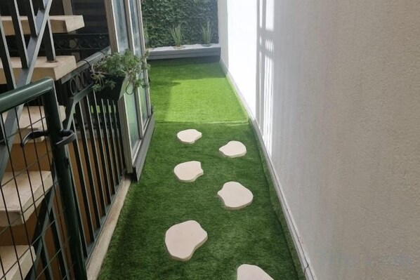 A narrow balcony with artificial grass and stepping stones, a metal railing, and a potted plant. - Apartment Centre Carmes (Toulouse)