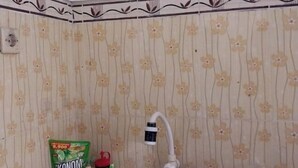 A bathroom with floral wallpaper, a showerhead, and a bag of Ekonomi detergent.