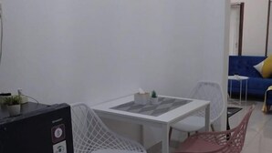 A room with a white table, two chairs, a black electronic device, a blue sofa, and a small white table with a plant.