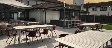 An outdoor patio with tables and chairs, a barbecue area, and a building in the background.