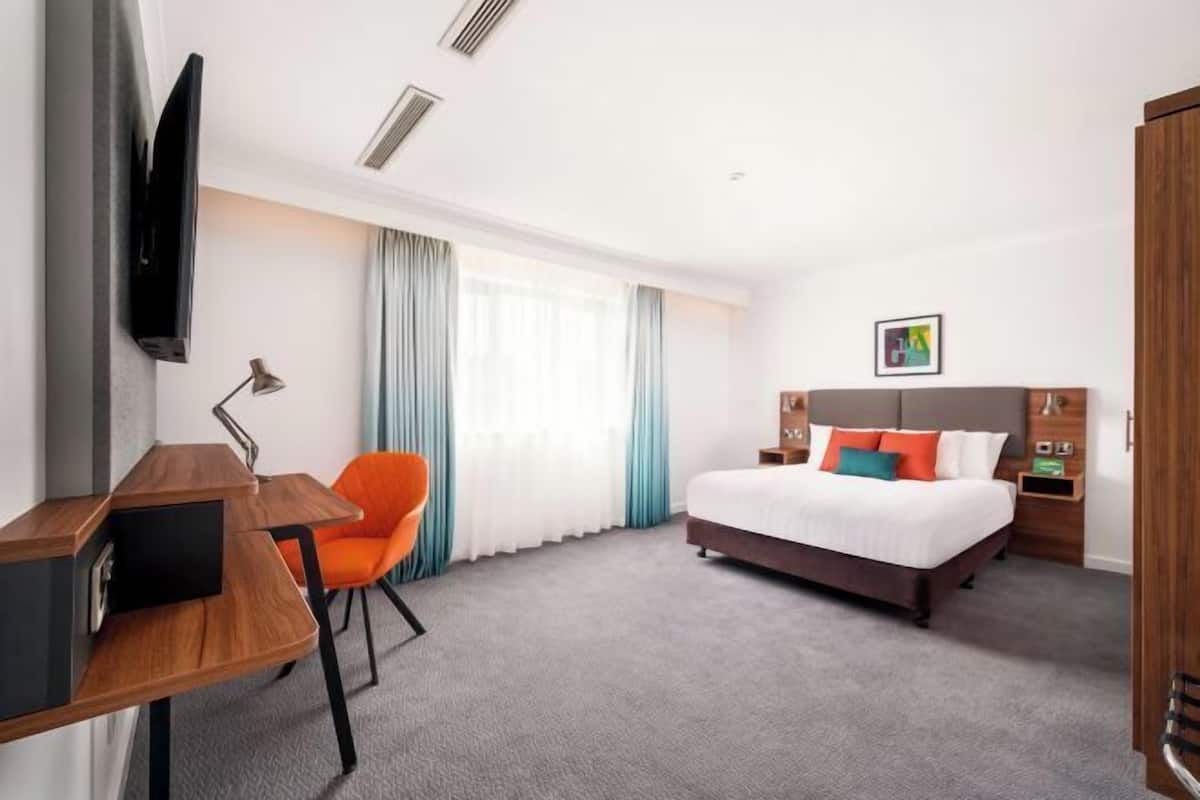A hotel room with a bed, desk, chair, and a TV mounted on the wall.