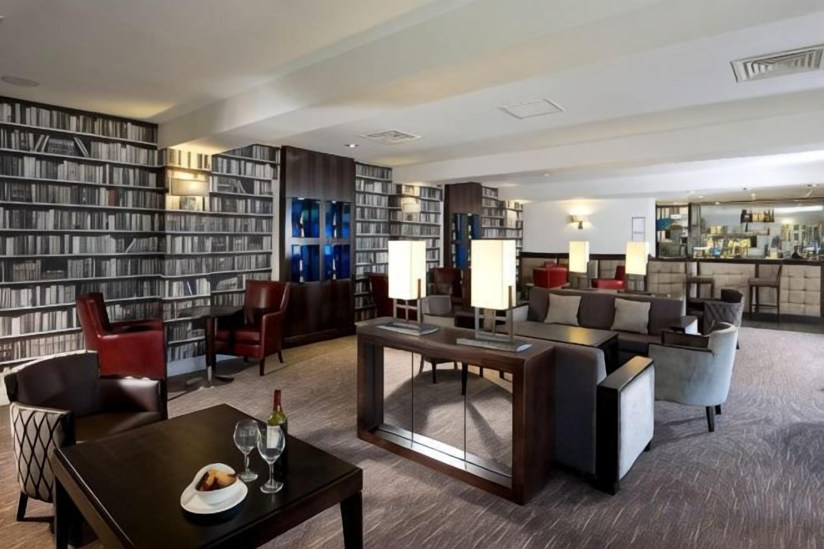 A hotel lobby with a large bookshelf, seating area, and a bar.