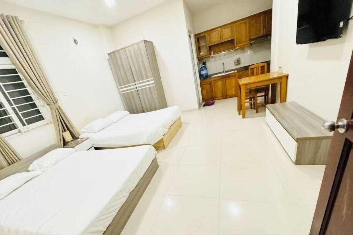 A hotel room with two beds, a kitchenette, a dining table, and a TV mounted on the wall.